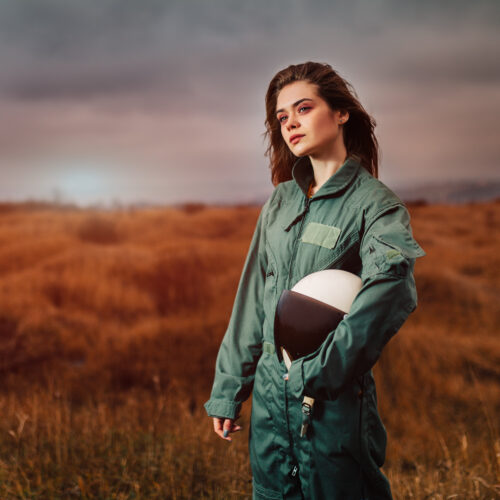 portrait of young beautiful girl pilot in uniform in the sunset field with helmet in hand